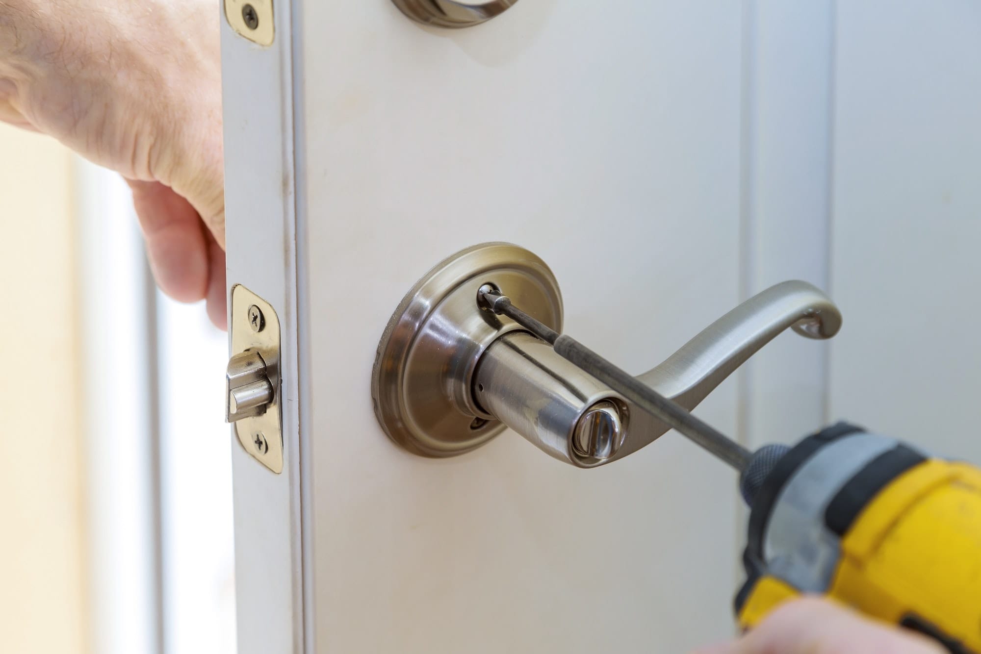 Close-up of hands installing a door handle with a power drill.