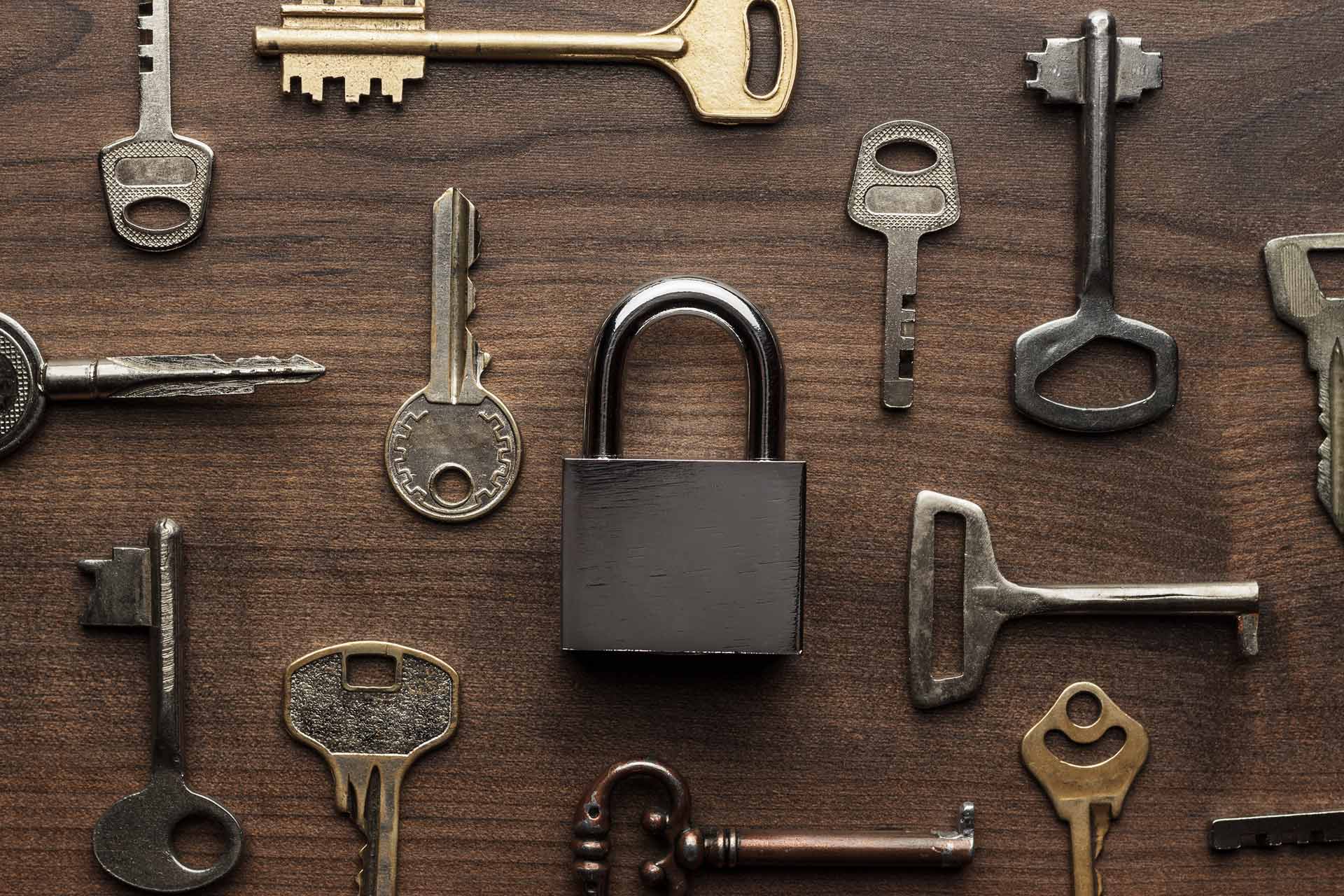 A black padlock surrounded by various old keys on a wooden surface.