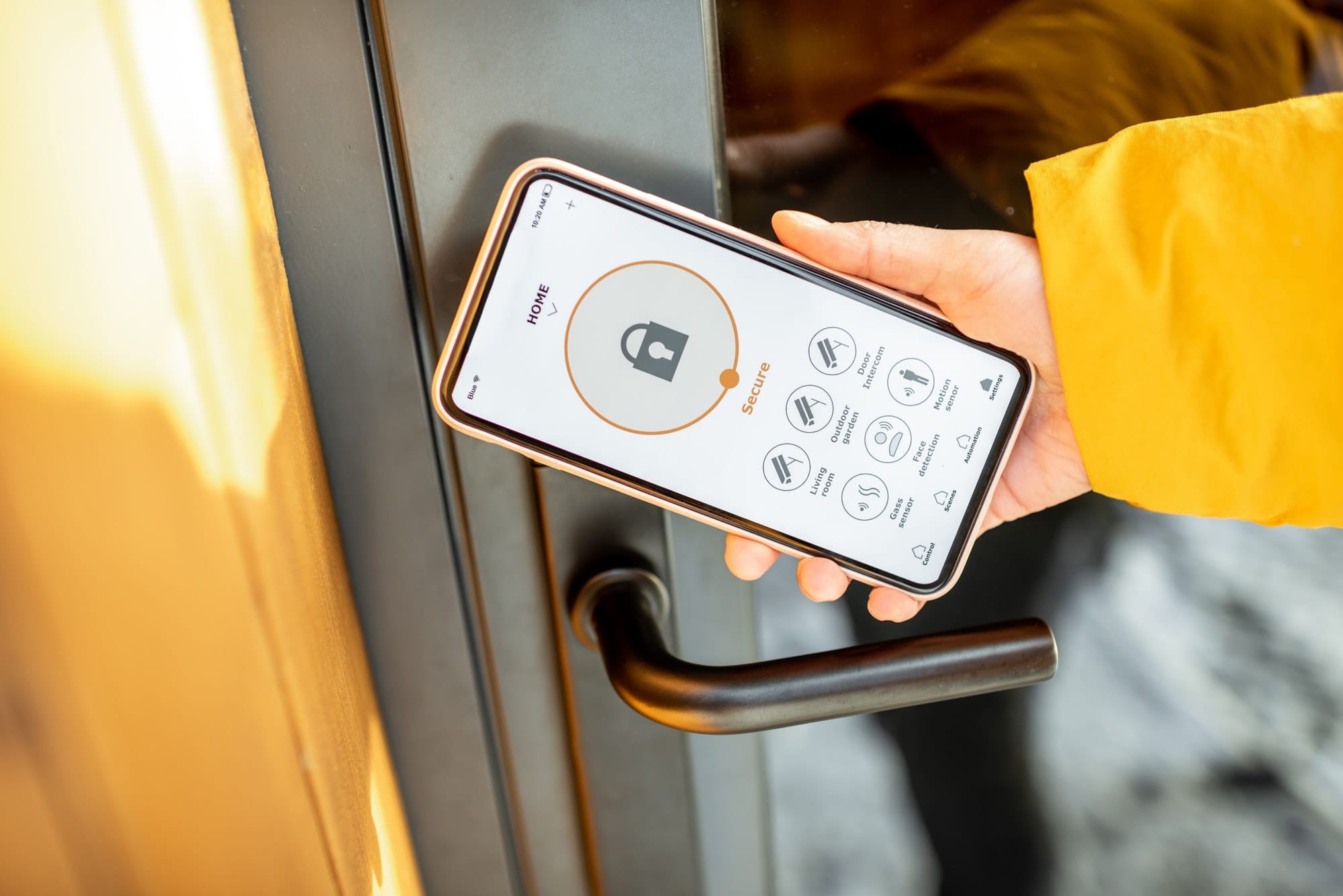 Hand holding a smartphone displaying a smart home security app near a door handle.