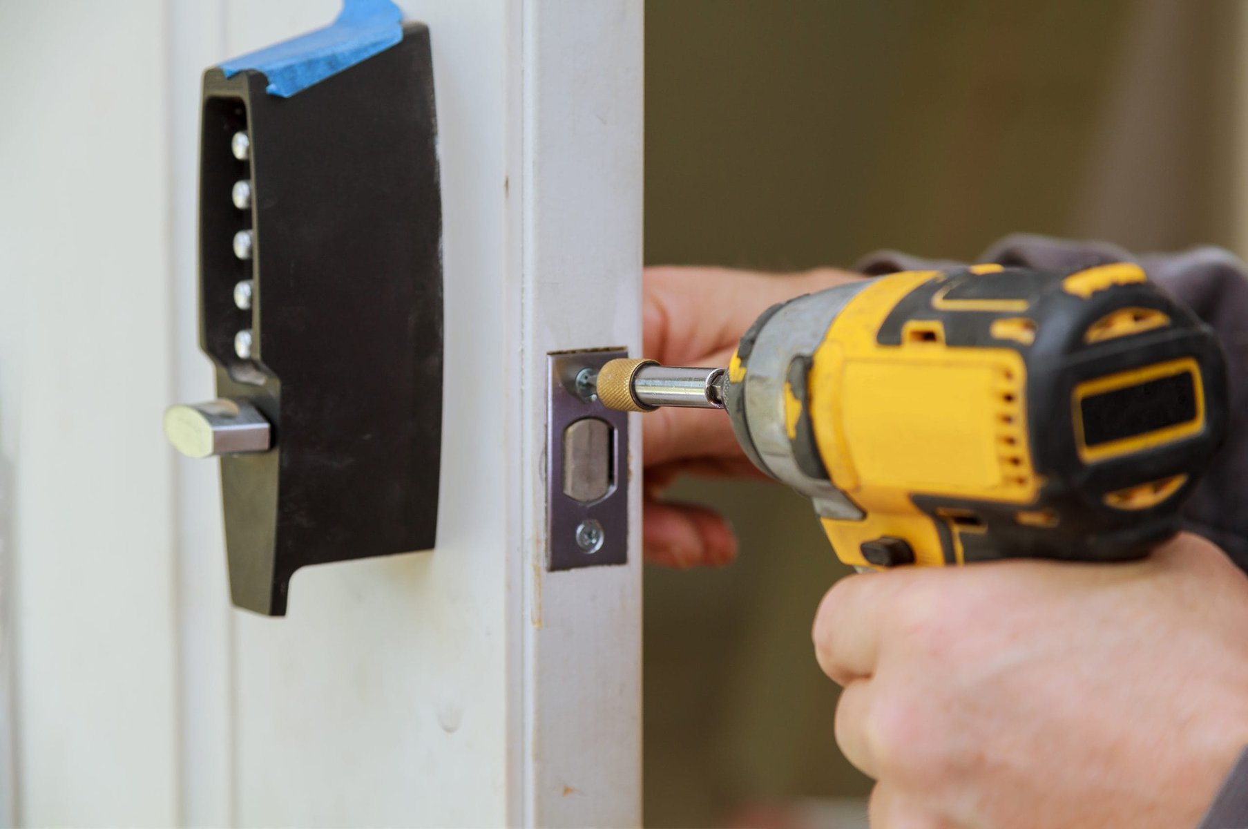 Close-up of hands using a power drill to install a door lock.