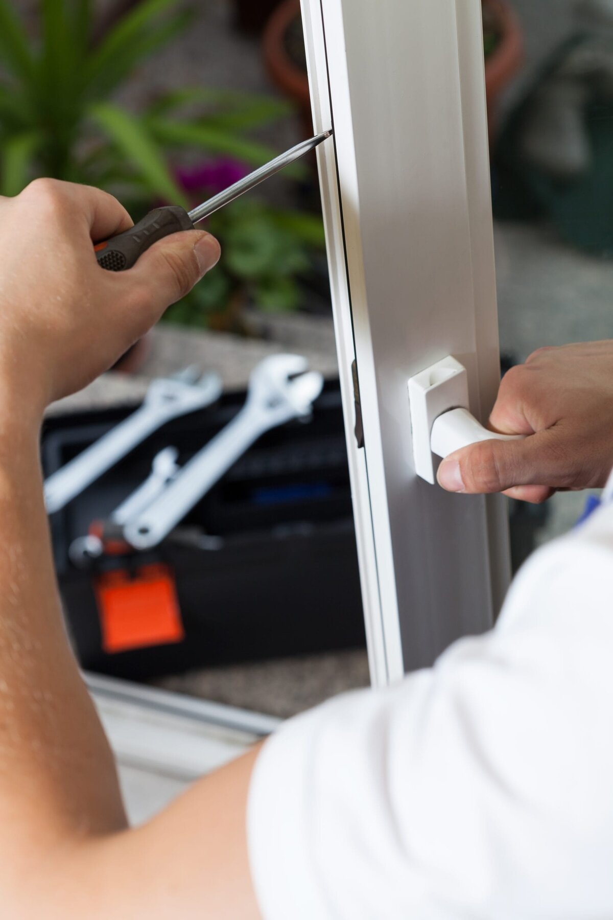 Close-up of hands repairing a white window frame with a screwdriver.