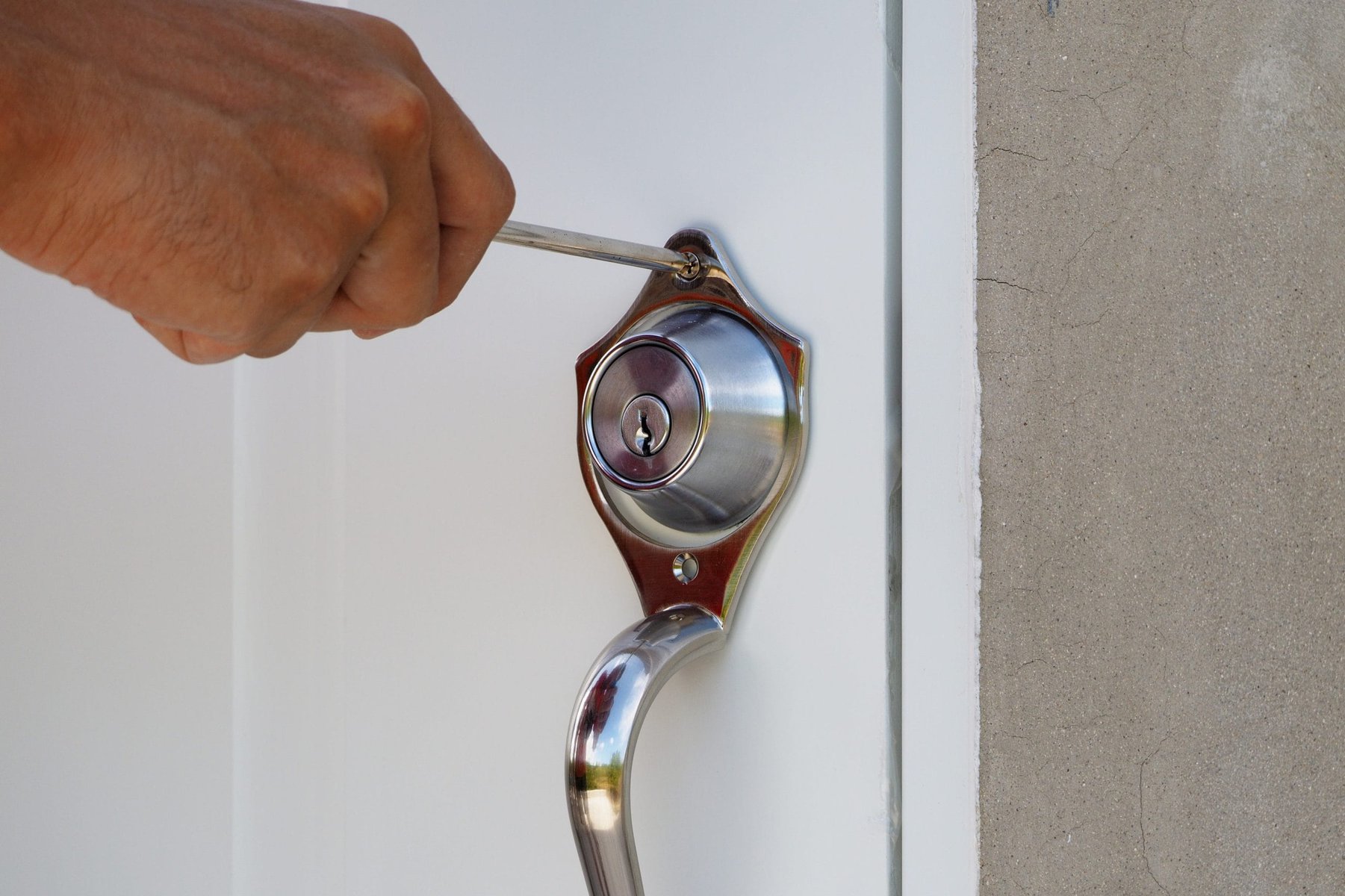 Hand using a screwdriver to tighten a silver door lock on a white door