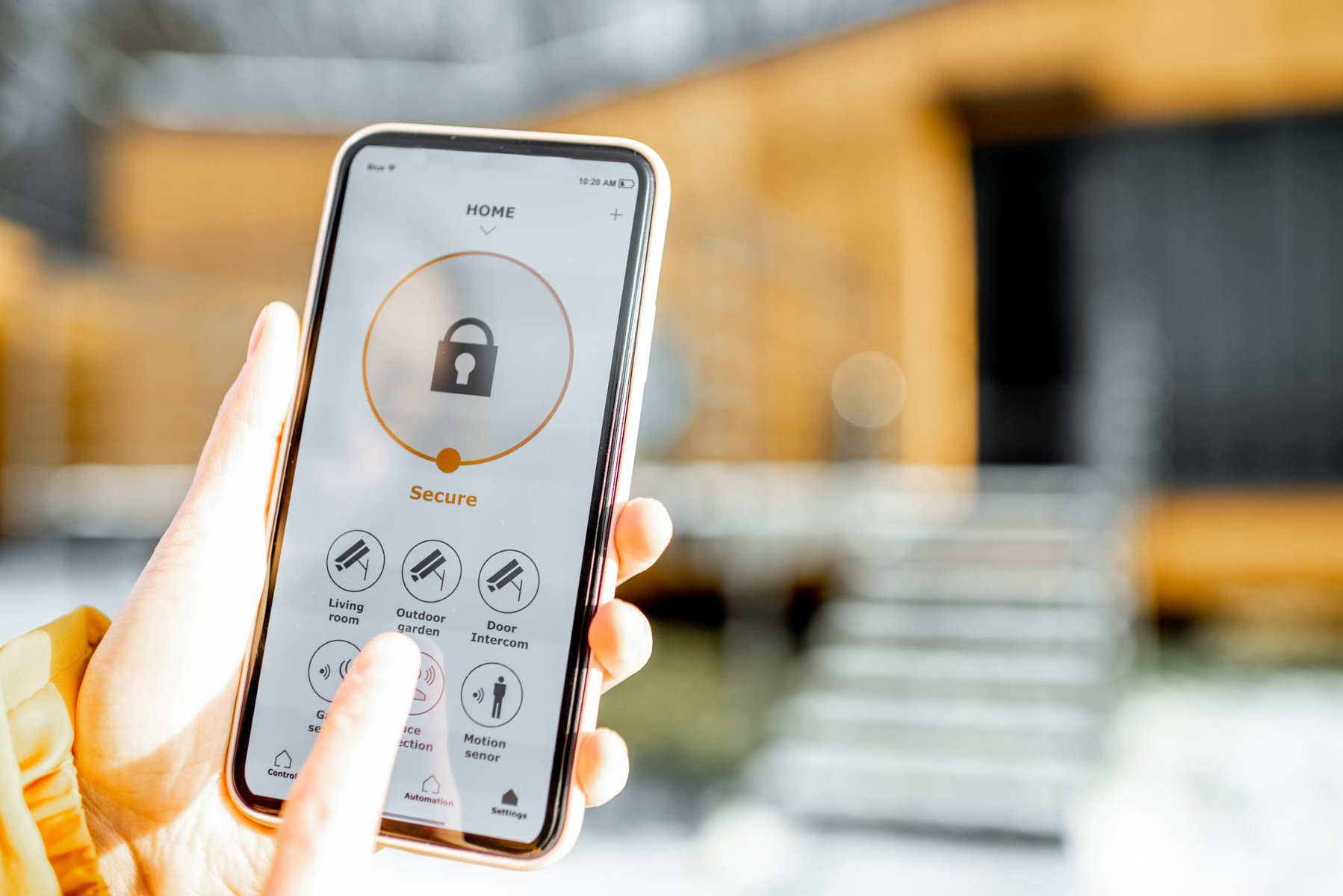 Hand holding a smartphone displaying a smart home security app.