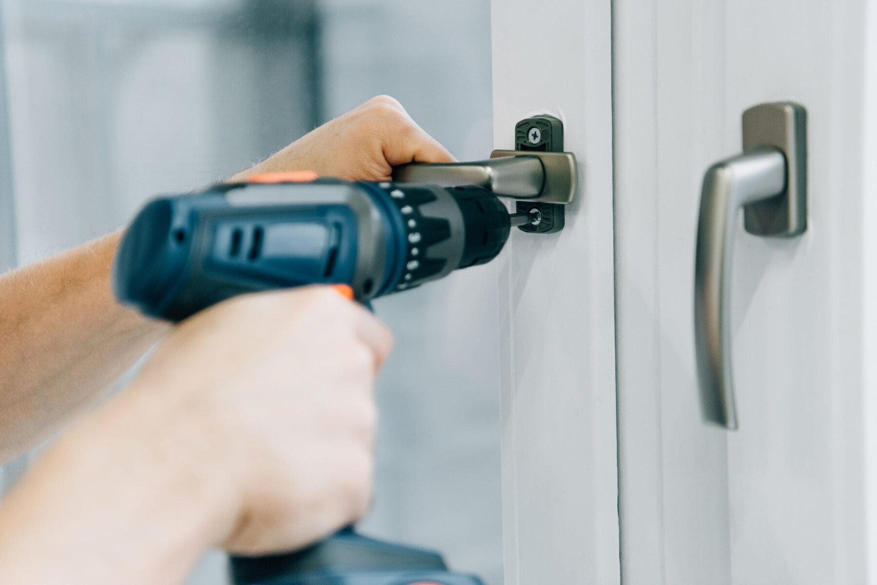 Close-up of hands using a power drill to install a window handle.