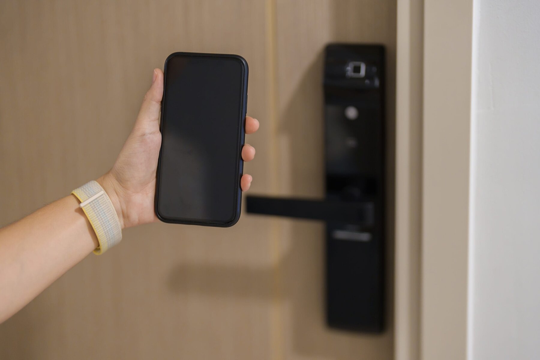 Hand holding a smartphone near a black digital door lock