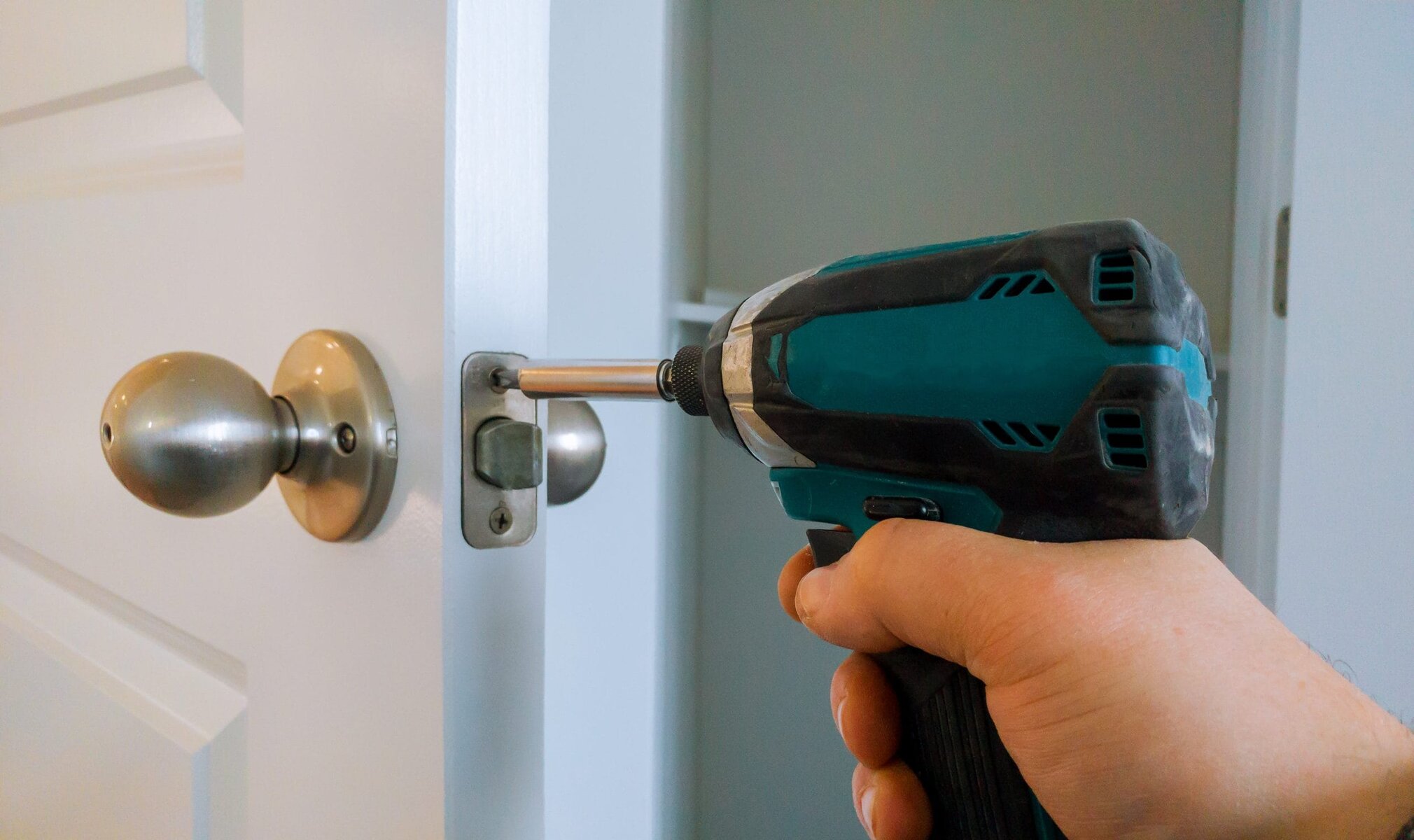 Hand using a power drill to install a doorknob on a white door.