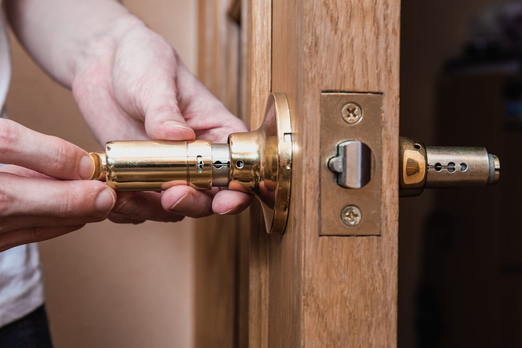 Hands installing a golden door handle into a wooden door.