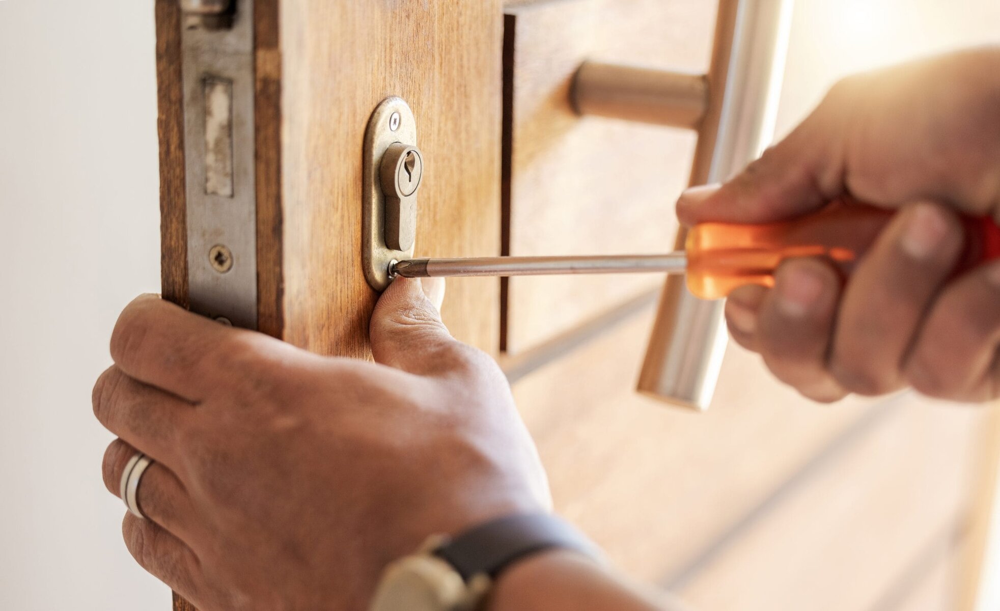 Close-up of hands using a screwdriver to fix a door lock.