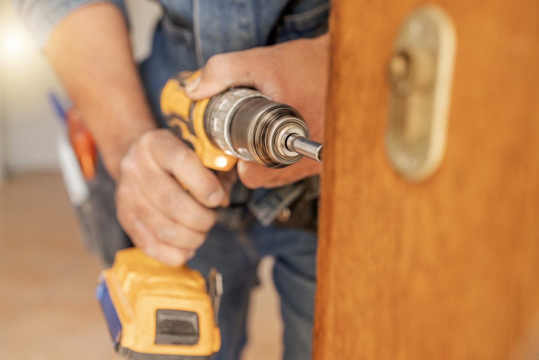 Person using a yellow cordless drill on a wooden door.
