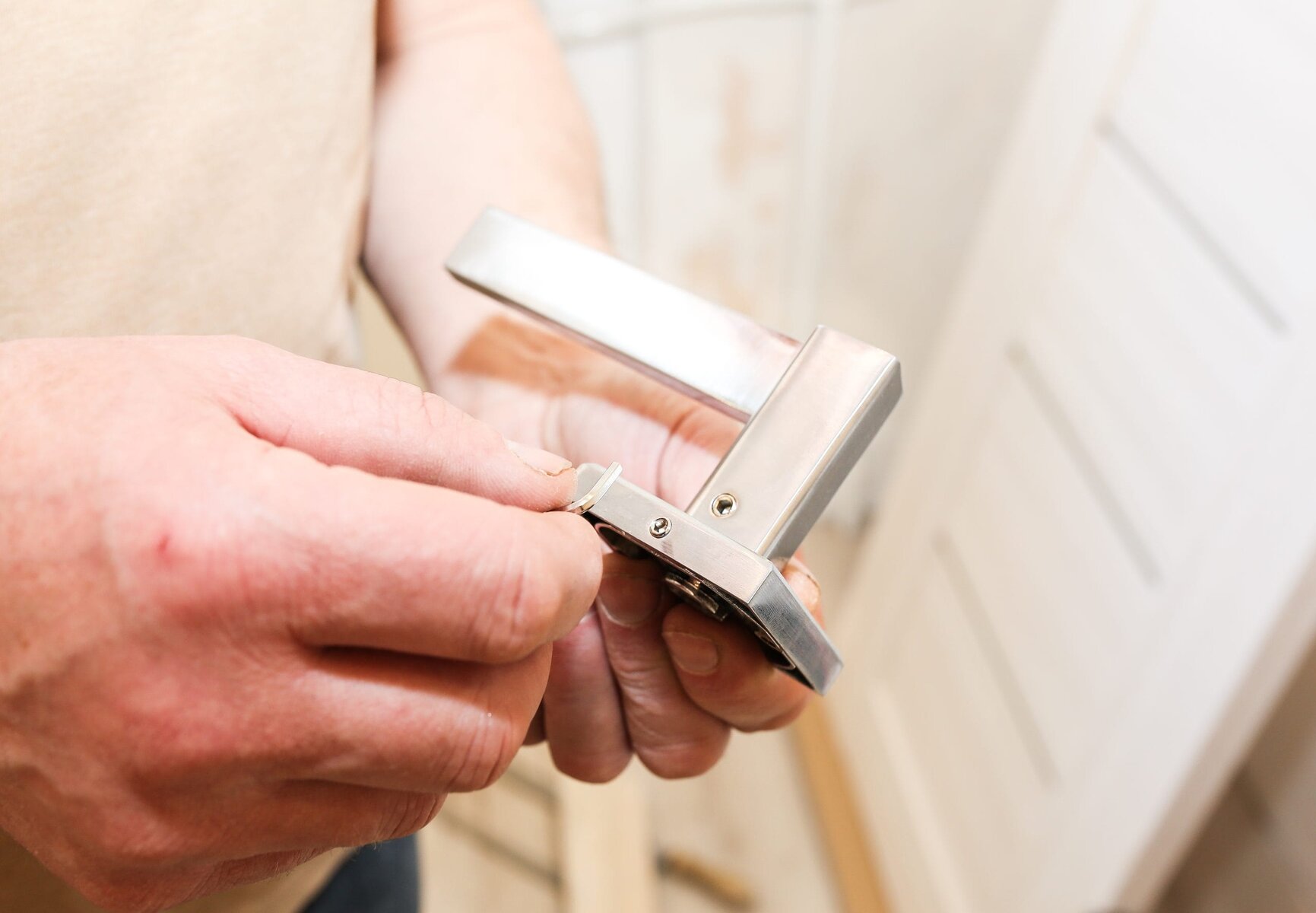 Close-up of hands installing a silver door handle on a white door.