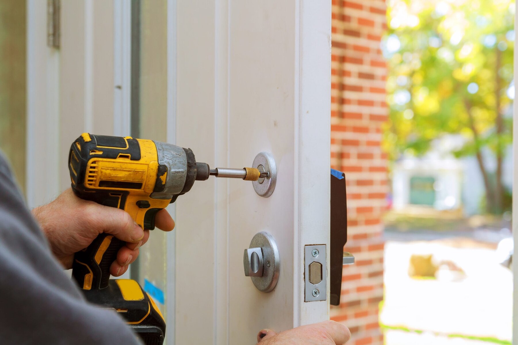 Close-up of hands using a power drill to install a door lock.