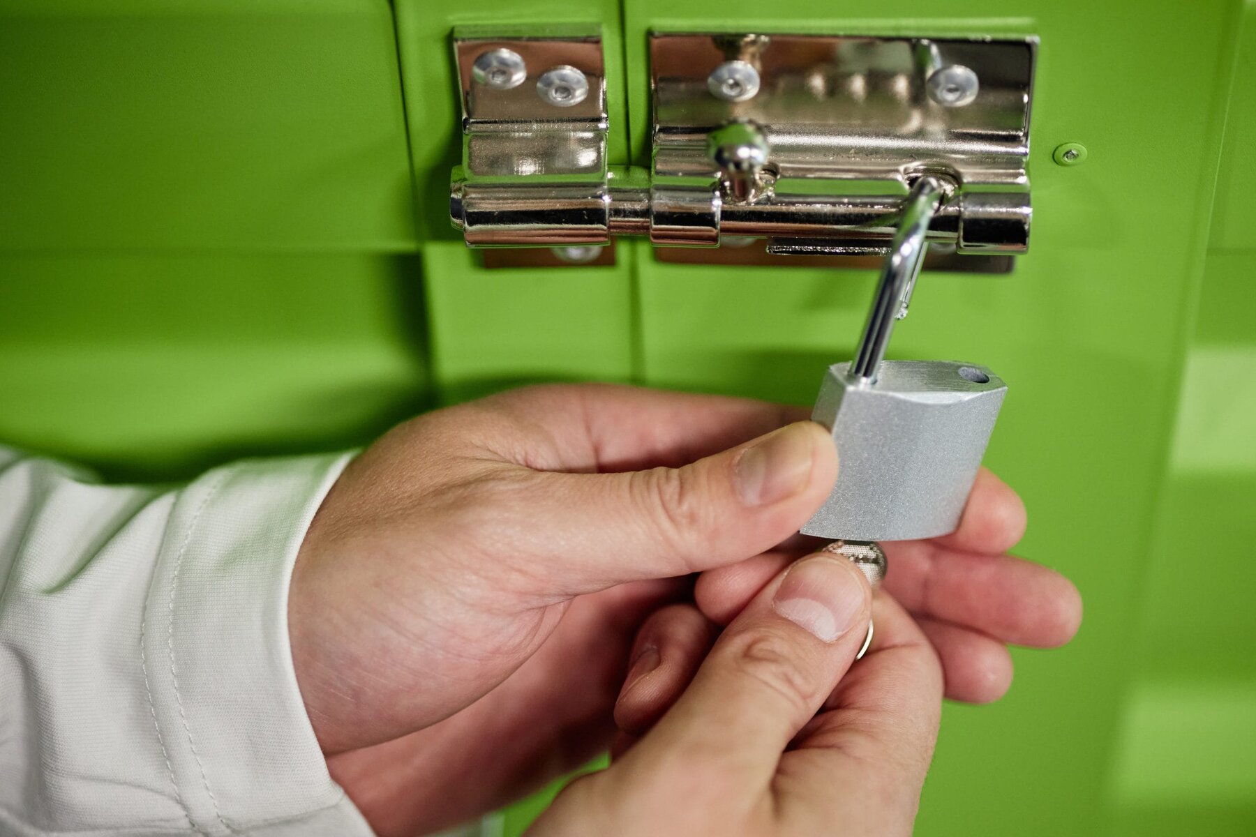 Hands locking a green cabinet with a silver padlock and key