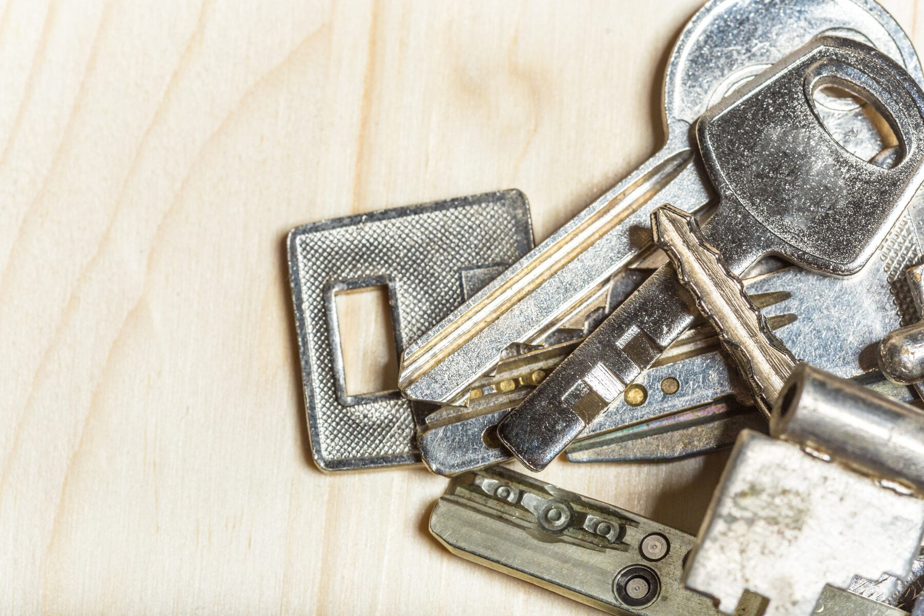 Close-up of a pile of various silver keys on a light wooden surface.
