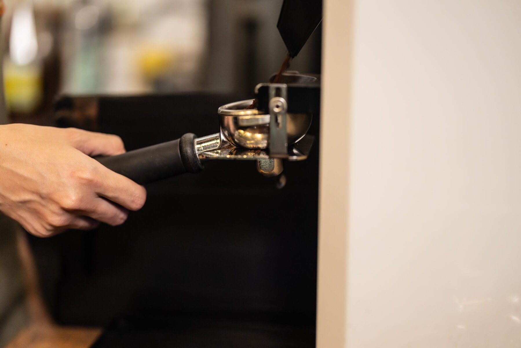 Close-up of a person's hands holding a portafilter under a coffee grinder.