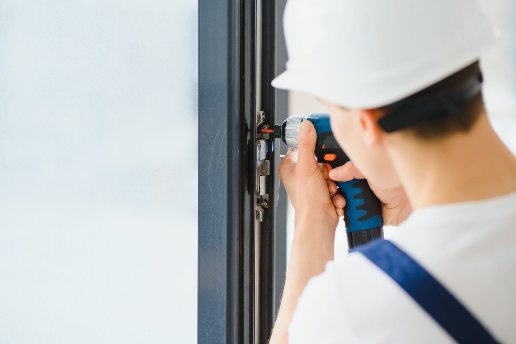 Worker in white hard hat using a power drill on a door frame.