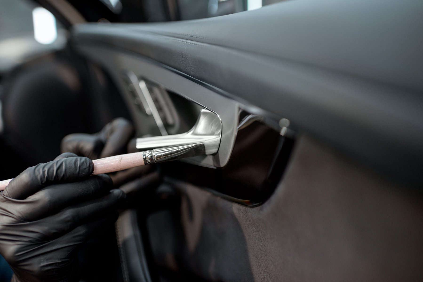 Person in black gloves cleaning a car door handle with a brush
