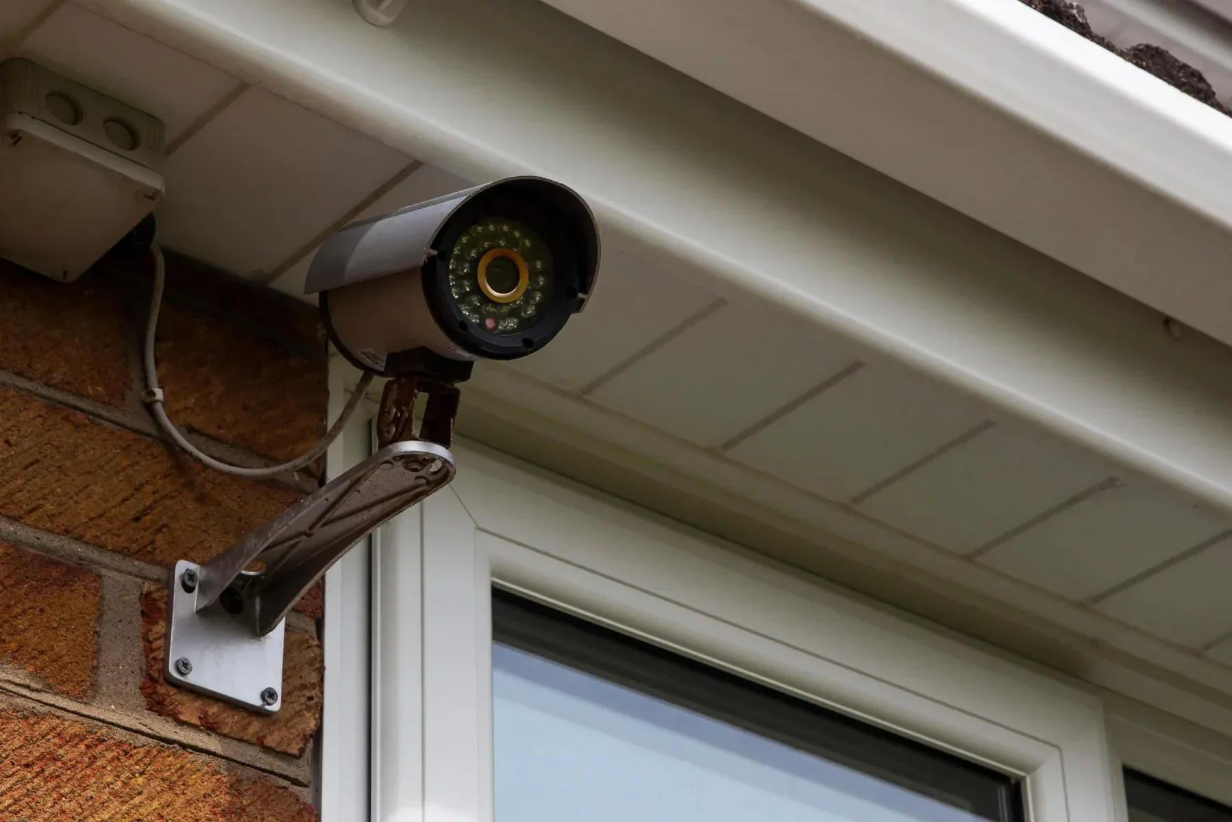 Security camera mounted on a brick wall under a white soffit.