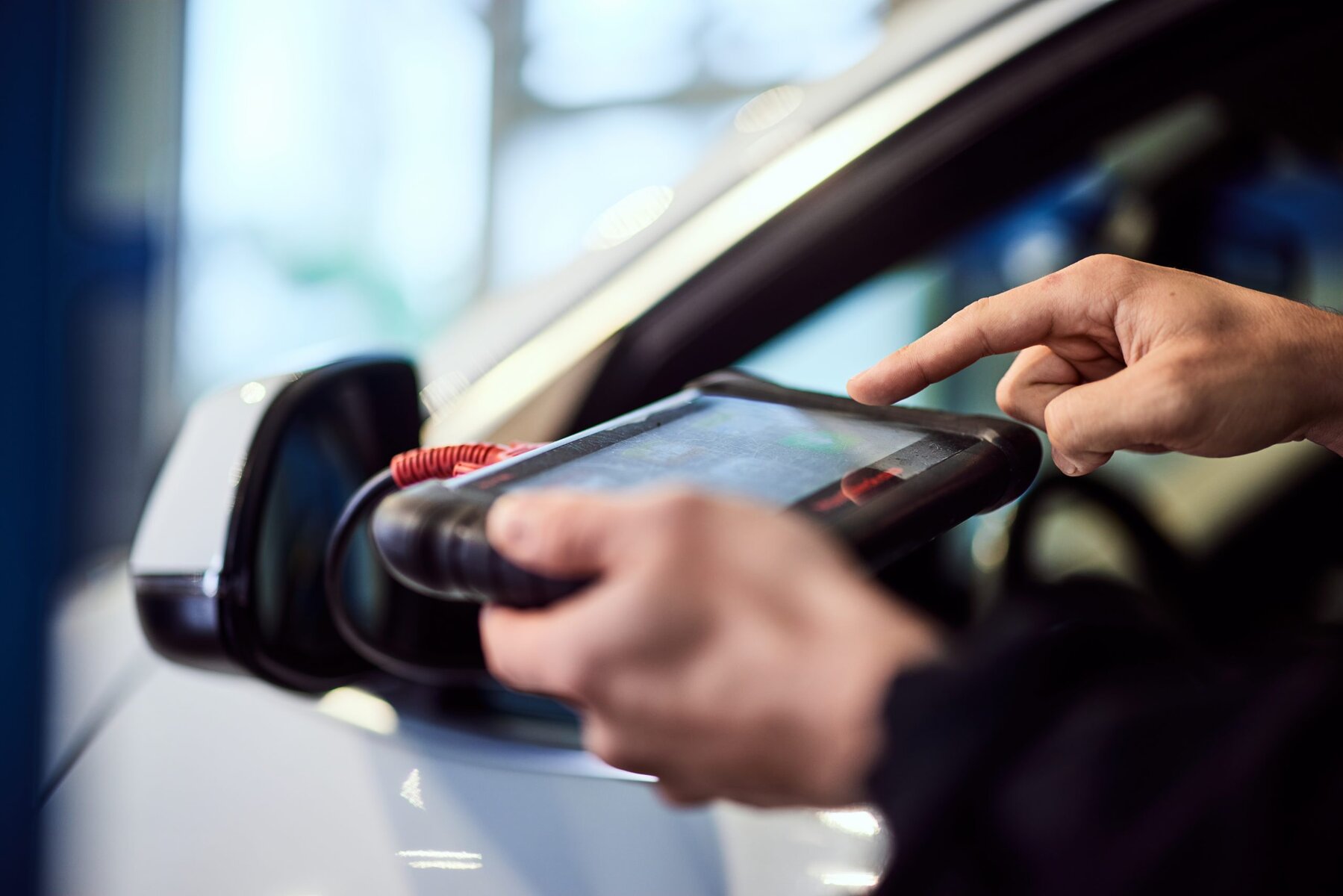 Close-up of a person's hands using a diagnostic tool on a car.