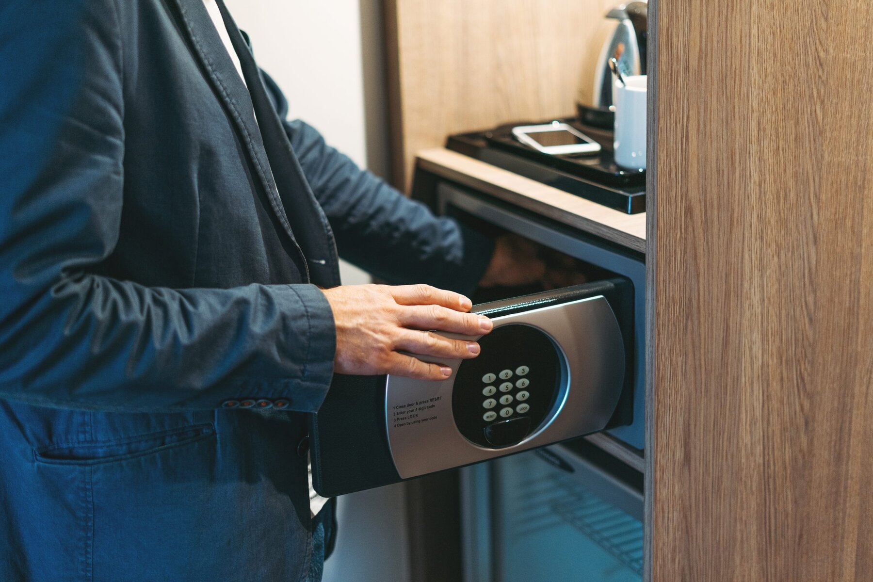 Man in a suit jacket opening a small hotel safe in a room.