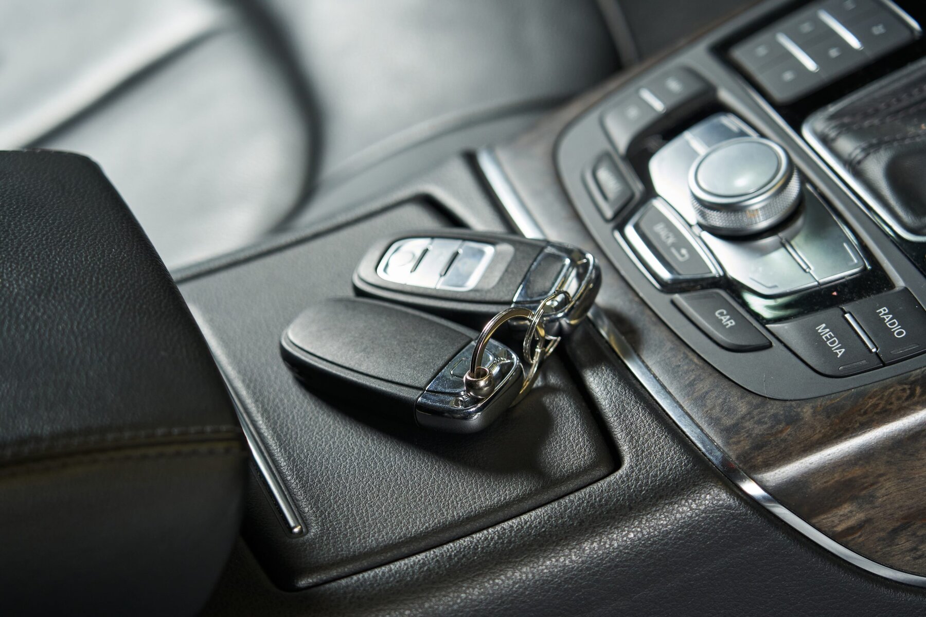 Two modern car keys resting on a black console inside a vehicle.
