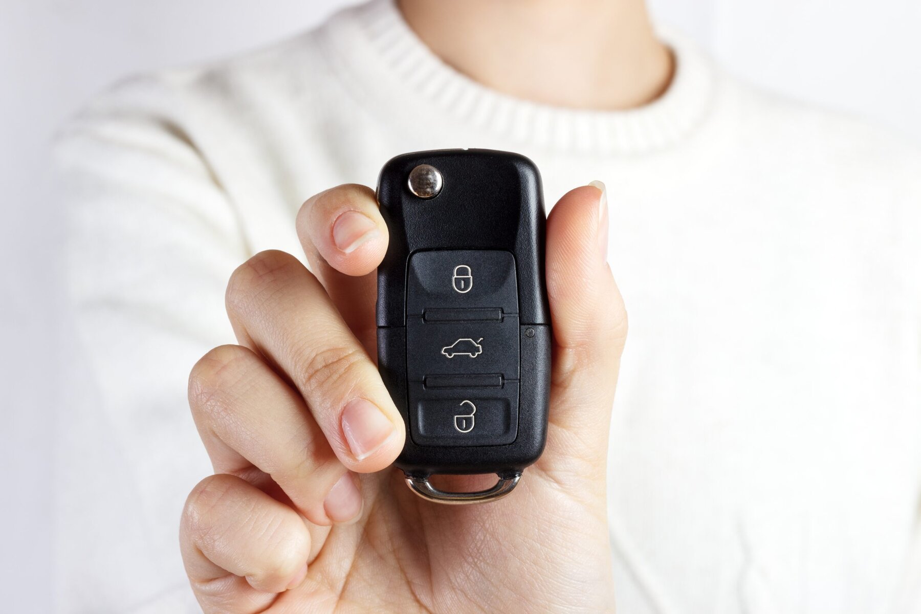 Hand holding a black car key with three buttons.