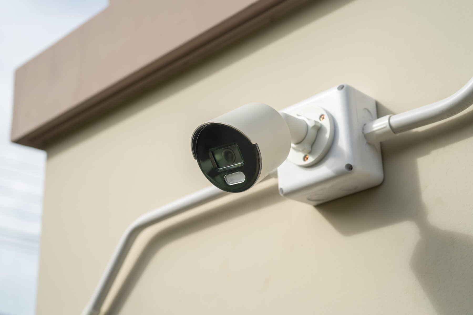 White security camera mounted on a beige wall with visible wiring.