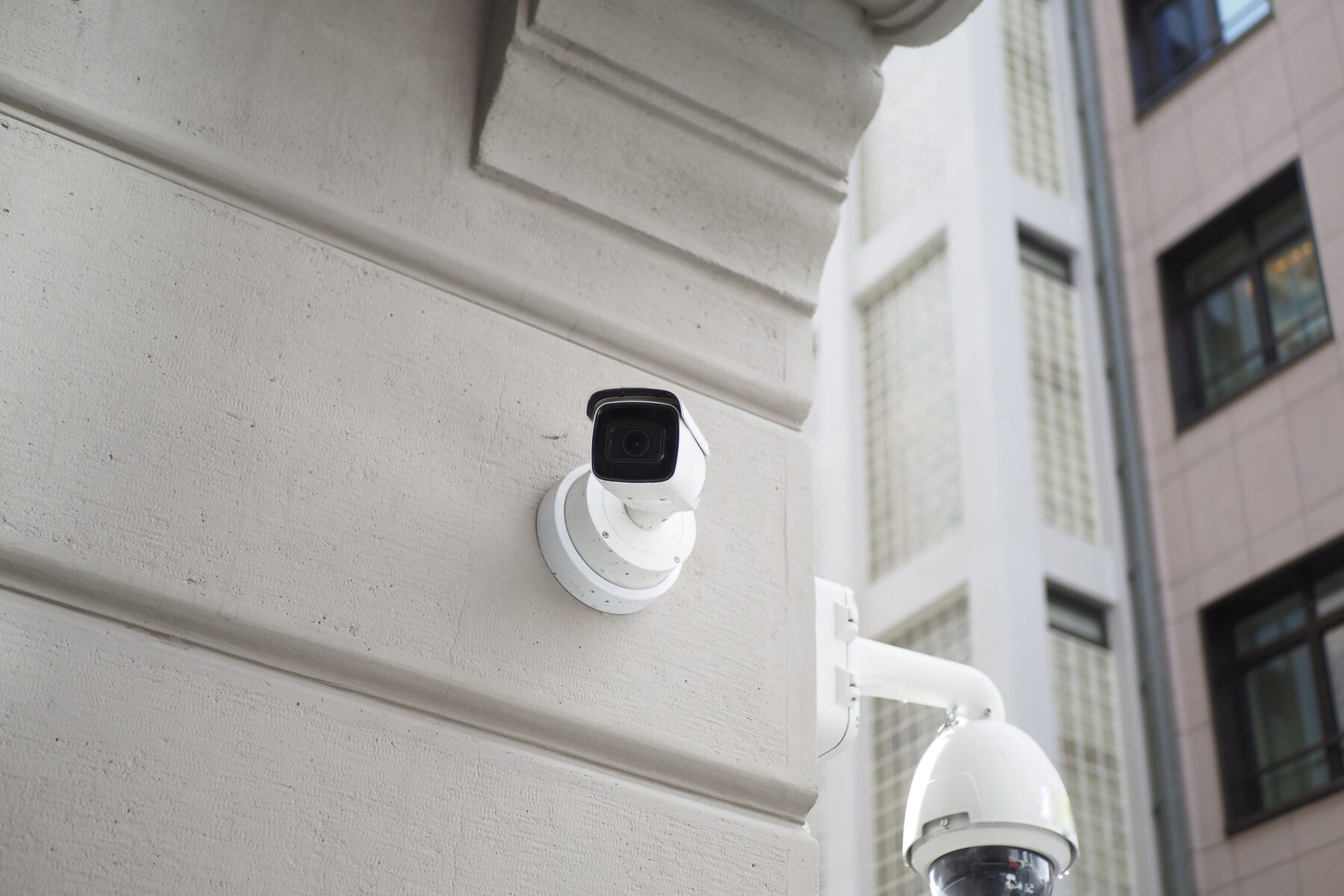 White security camera mounted on a building wall, with another camera below.