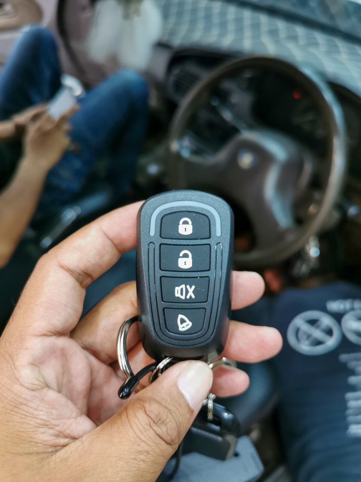 Hand holding a black car alarm remote with four buttons.