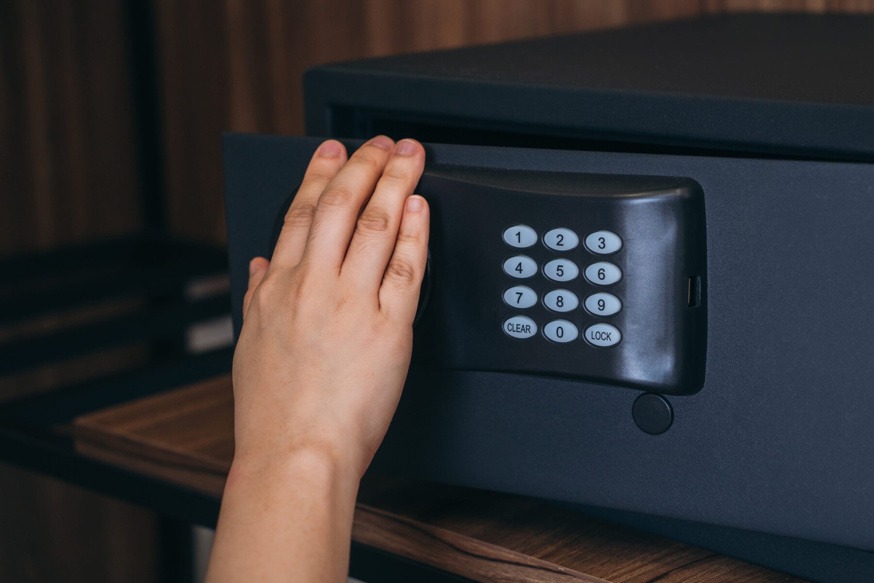 Hand opening a dark gray safe with a digital keypad.