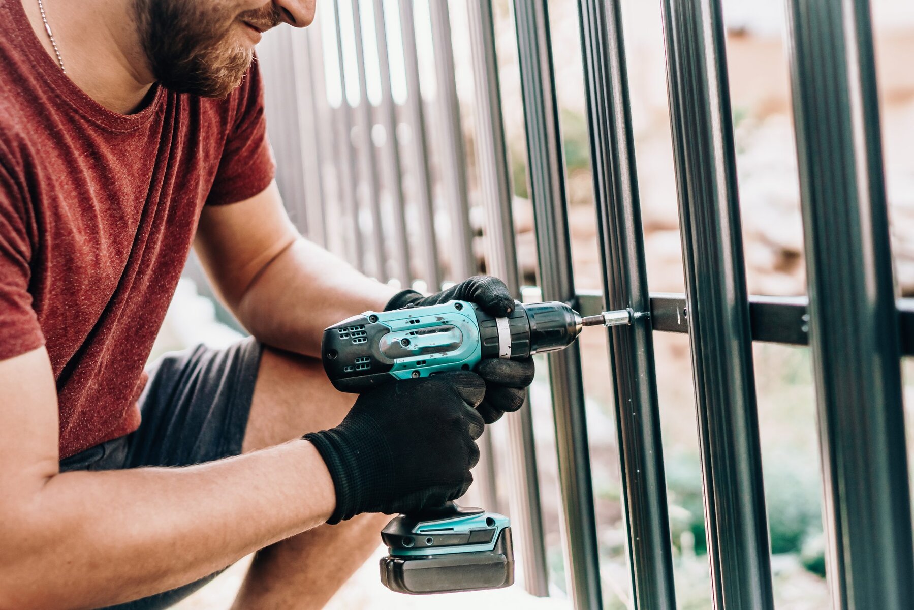 Man using a power drill to assemble a metal fence outdoors