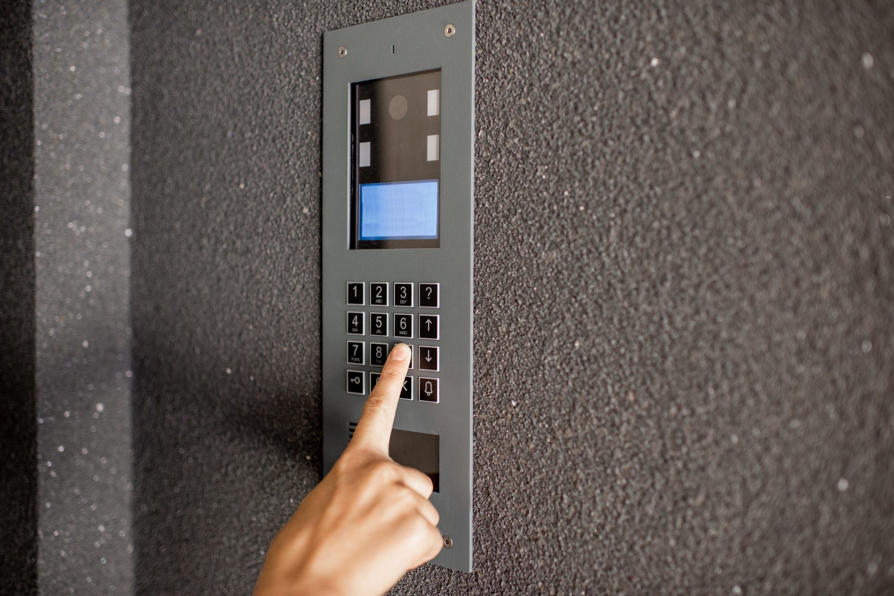 A person's finger pressing a button on a gray intercom panel.