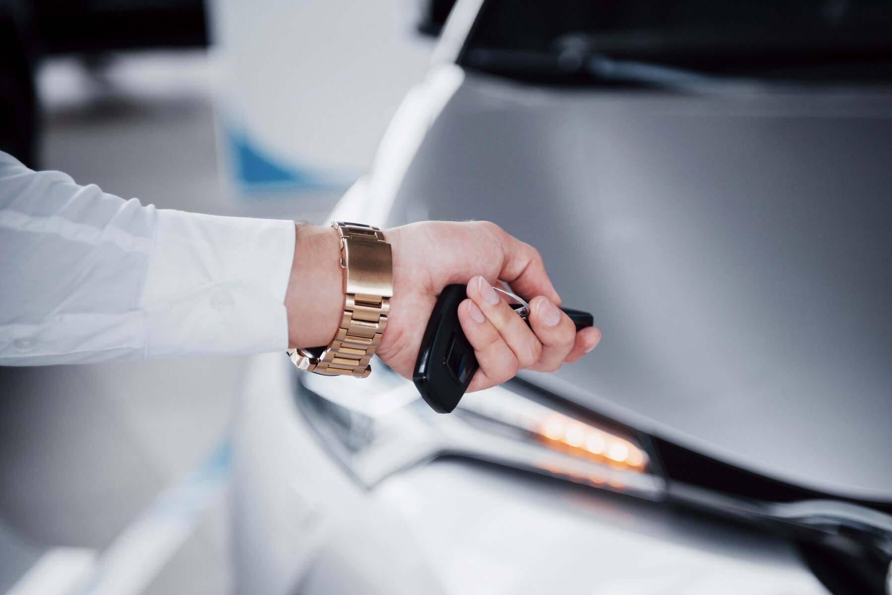 Man's hand with a gold watch holding car keys next to a car.
