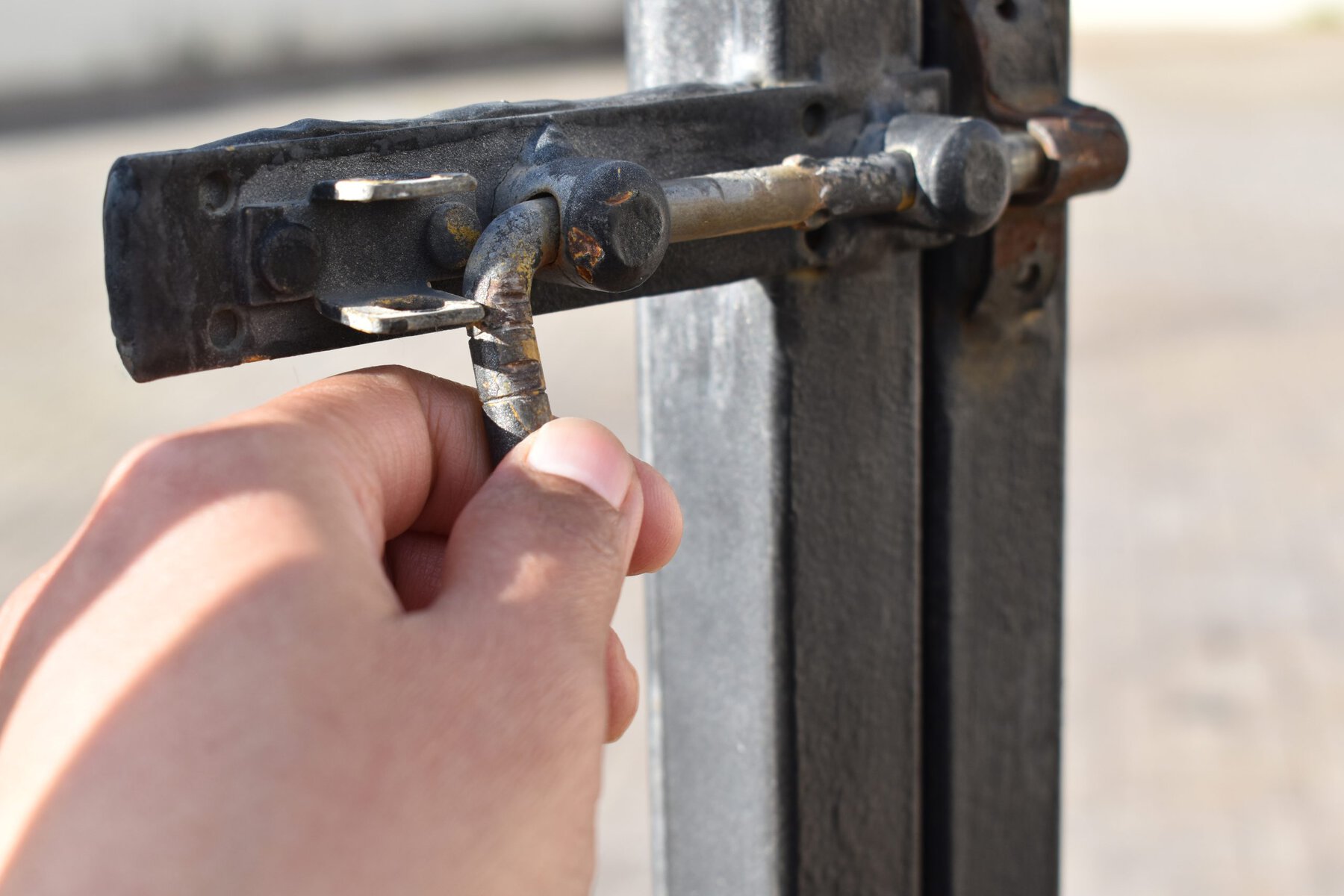 A hand operating a rusty metal gate latch in daylight.