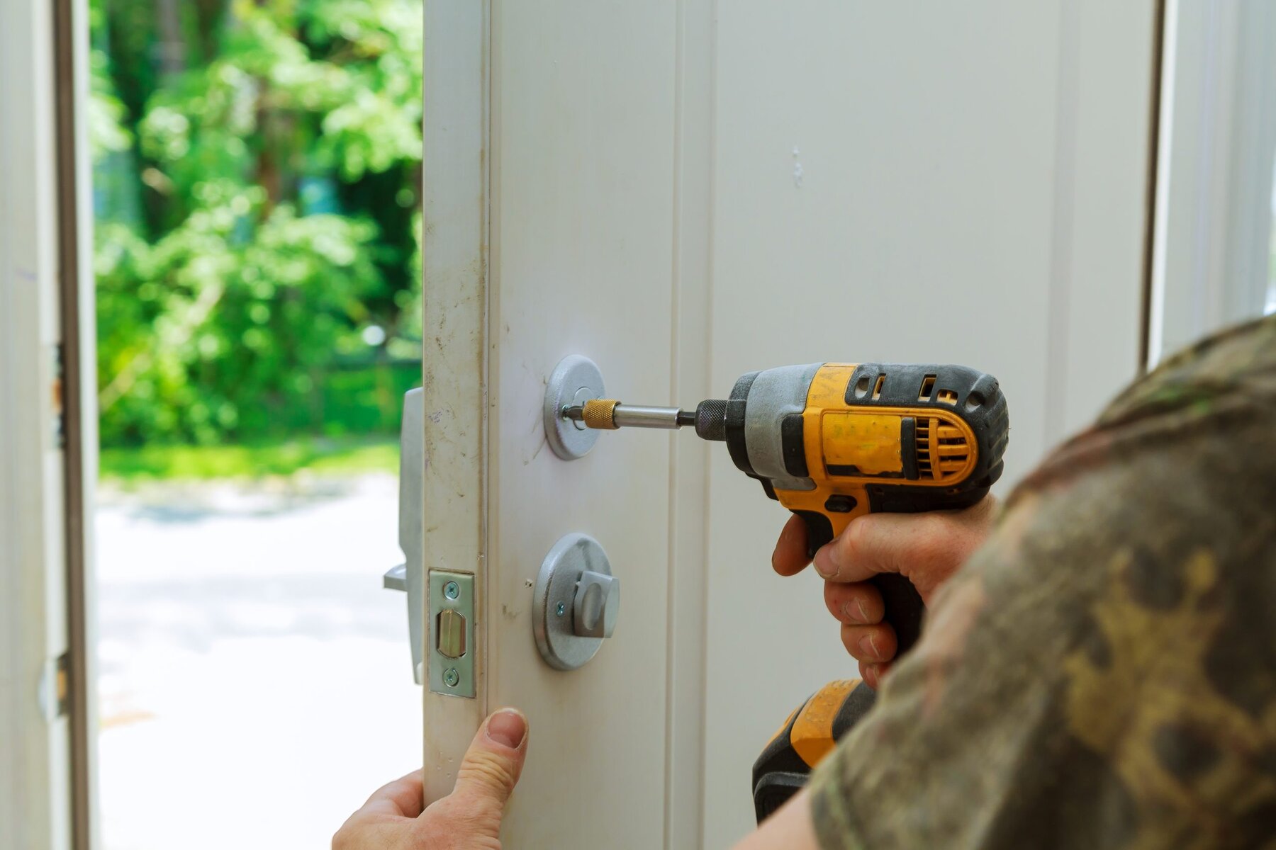 Person using a power drill to install a door handle on a white door.
