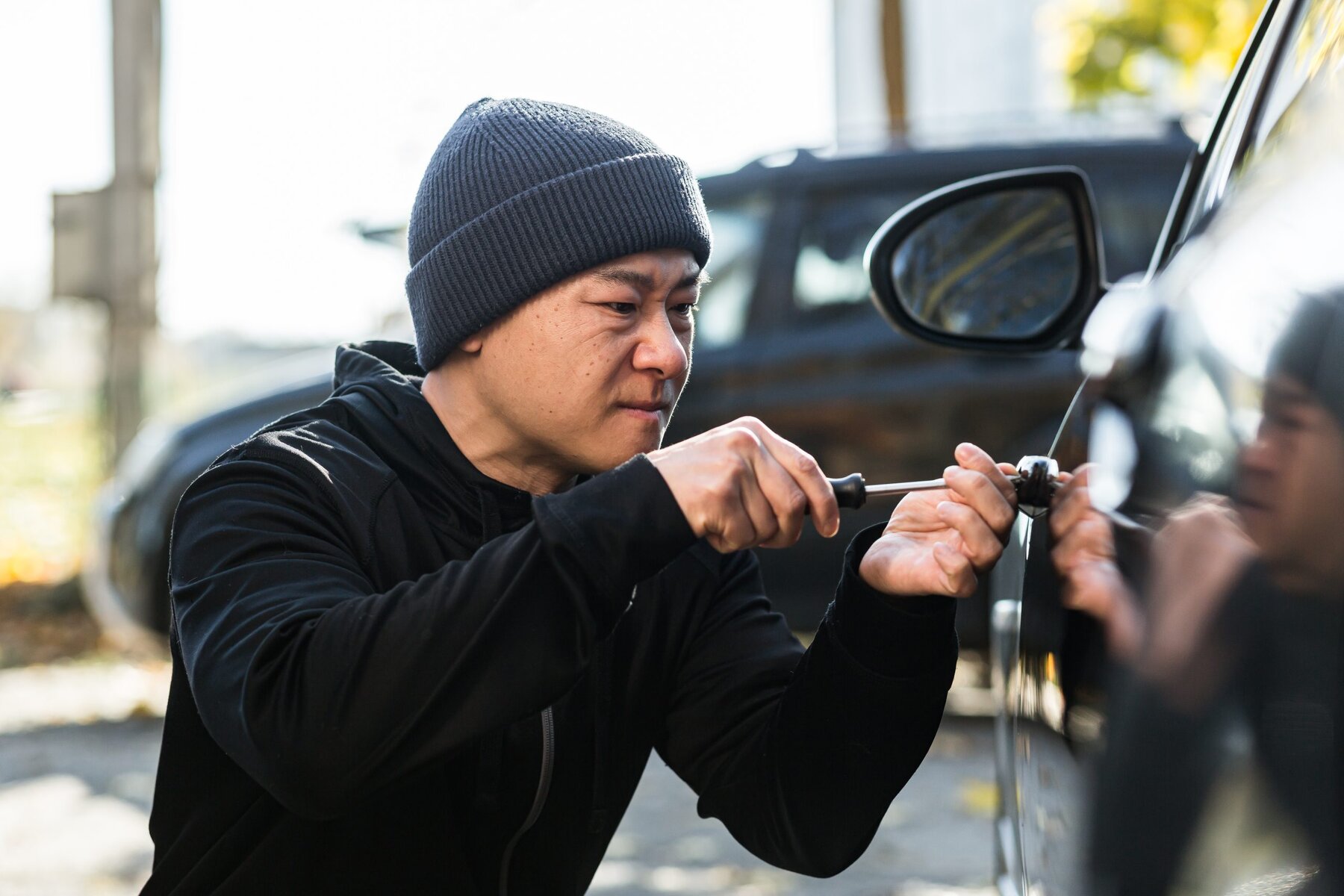 Man in a beanie using a screwdriver on a car door lock.