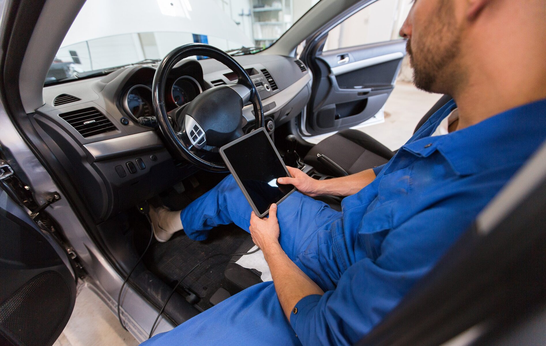 Mechanic in blue uniform sitting in a car and holding a tablet