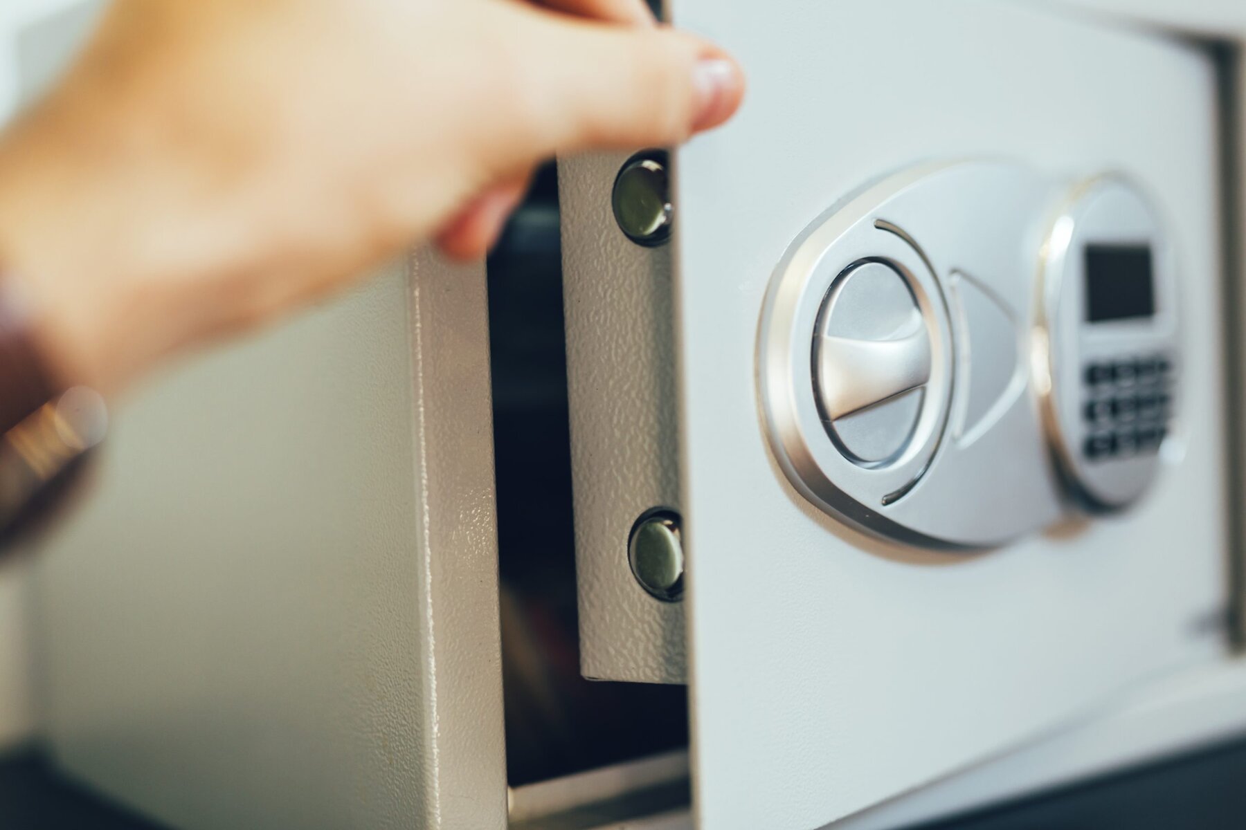 A hand opening a light gray safe with a digital keypad and a silver handle.