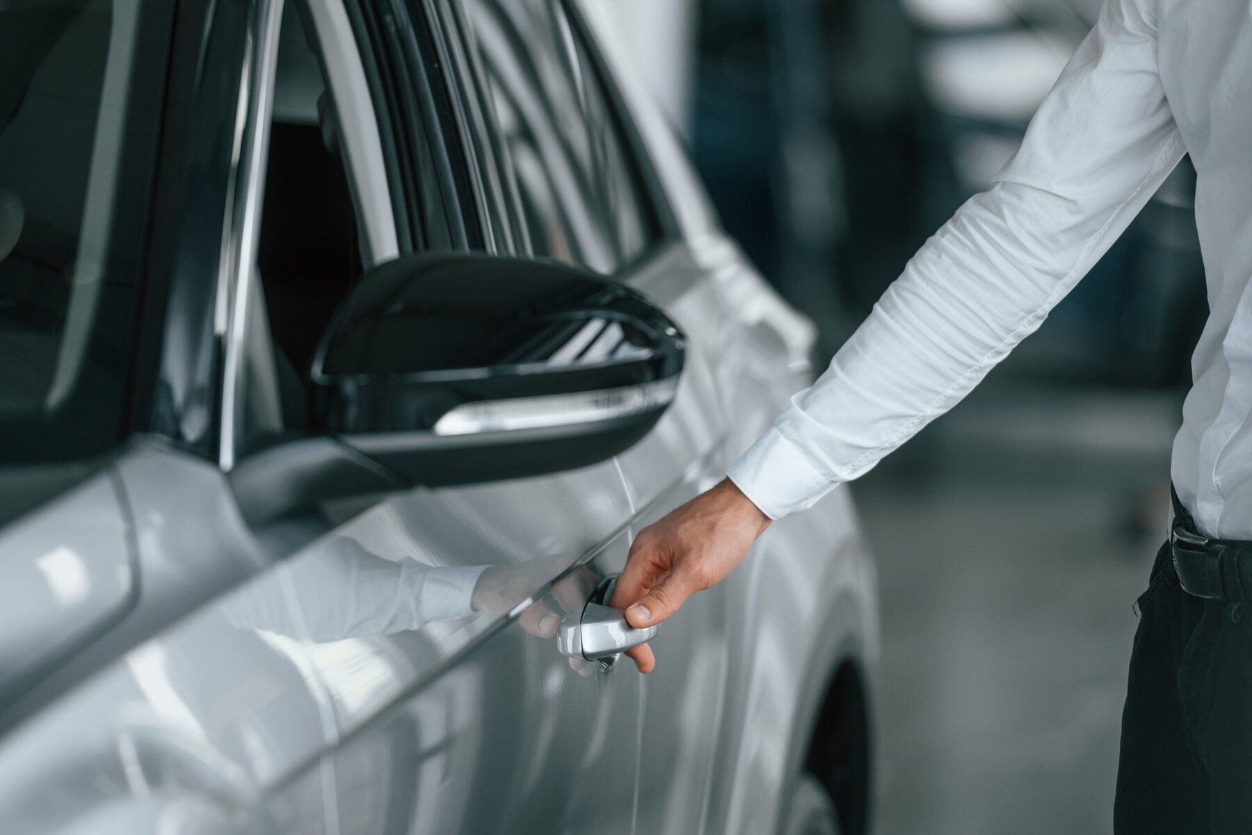 Man in white shirt opening the door of a silver car