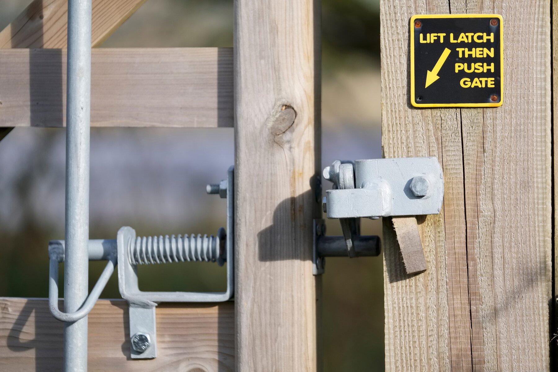 Close-up of a wooden gate with a metal latch and a yellow sign.