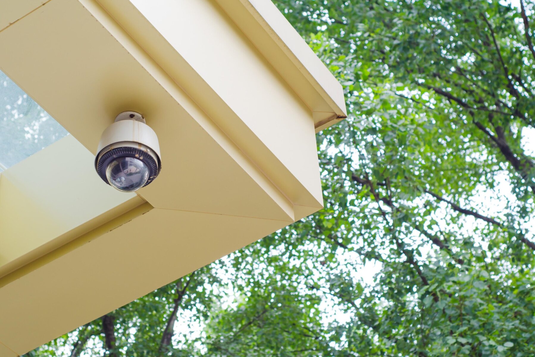 Security camera mounted on a building with green trees in the background.