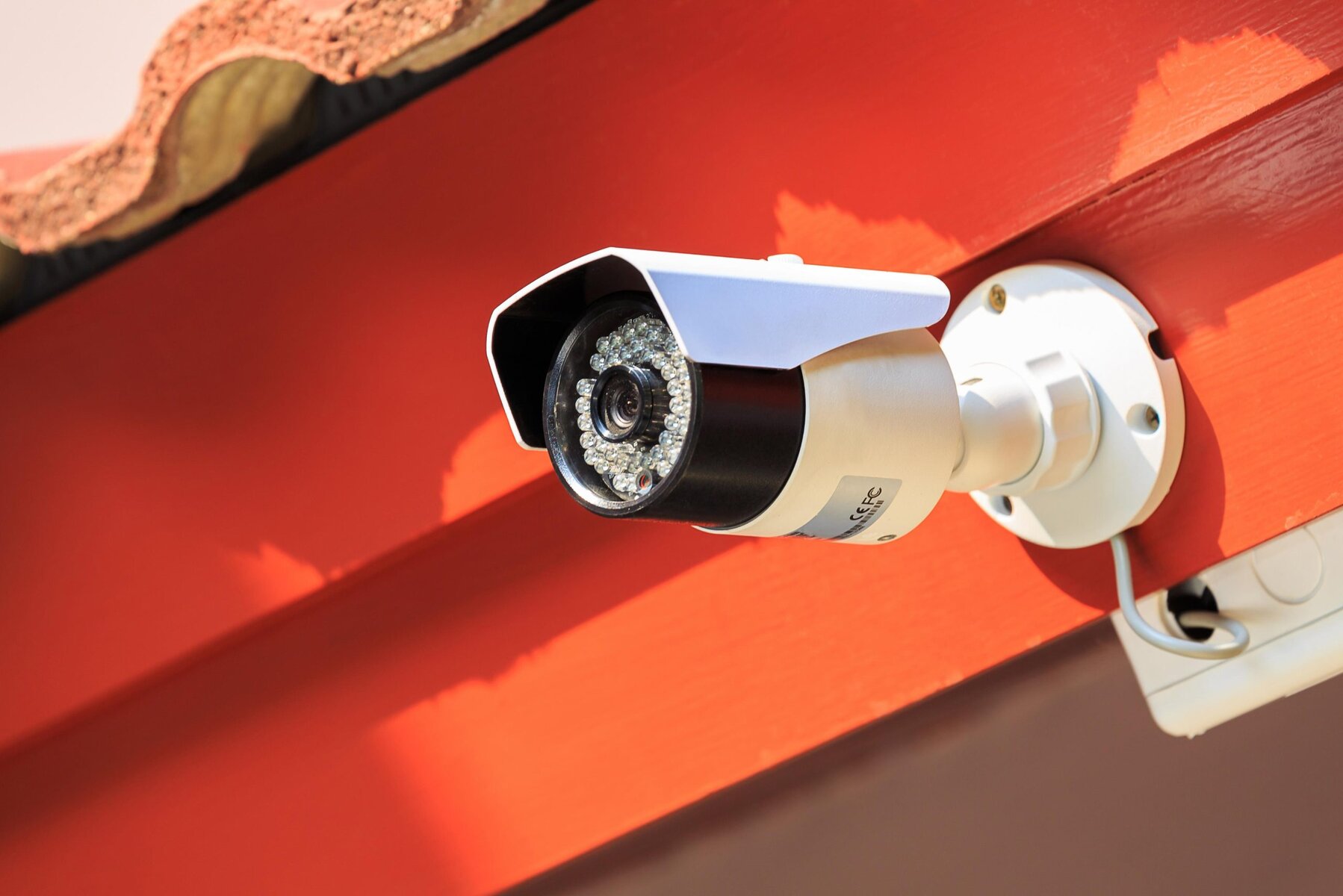 Close-up of a white security camera mounted on a red wall