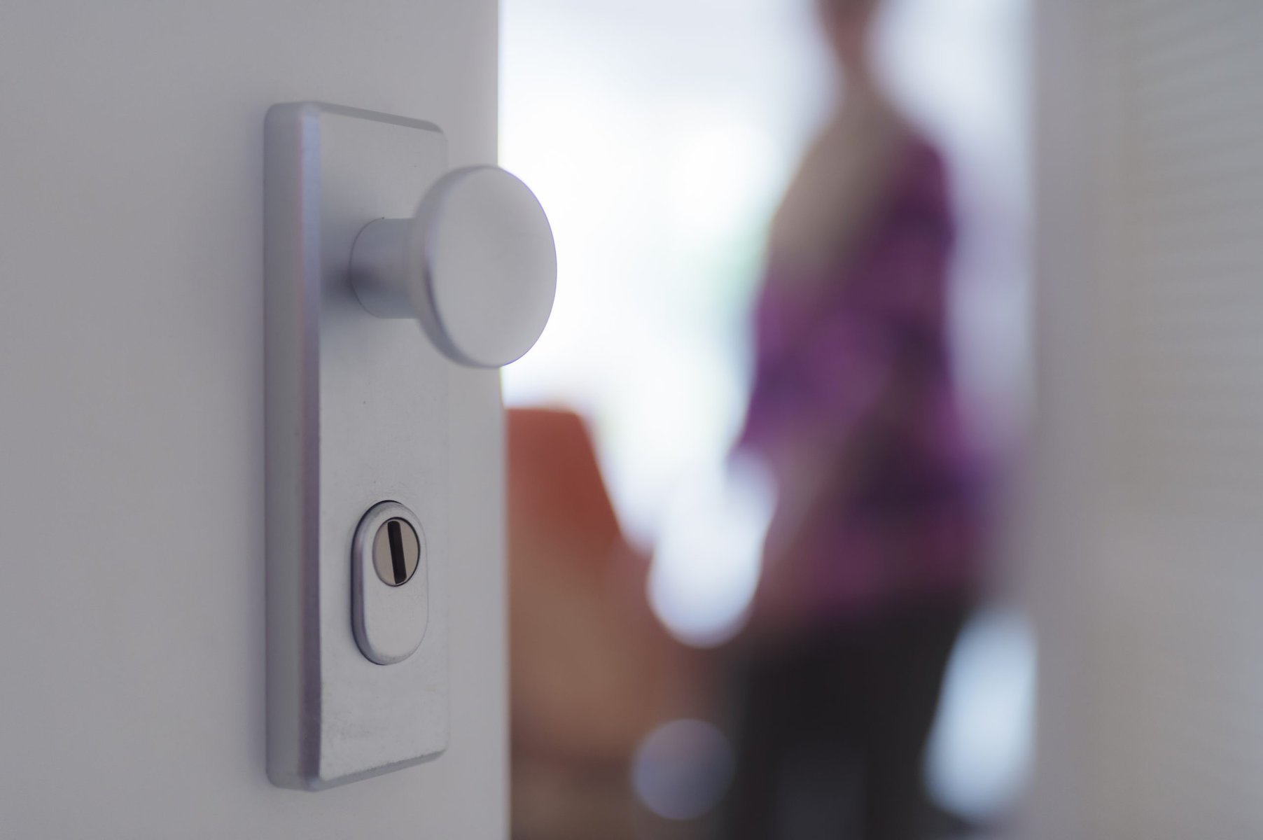 Close-up of a silver door handle and lock with a blurred person in the background.