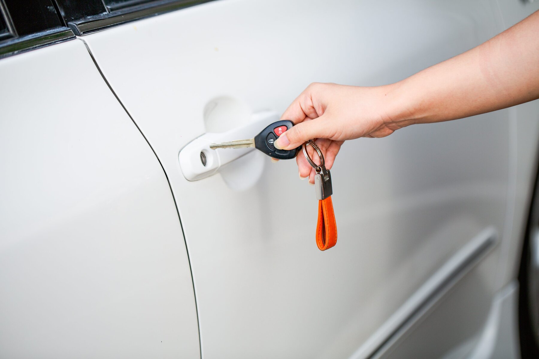 Hand inserting car key into door lock of a white car