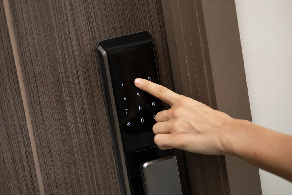 A hand entering a code on a black digital door lock on a wooden door.