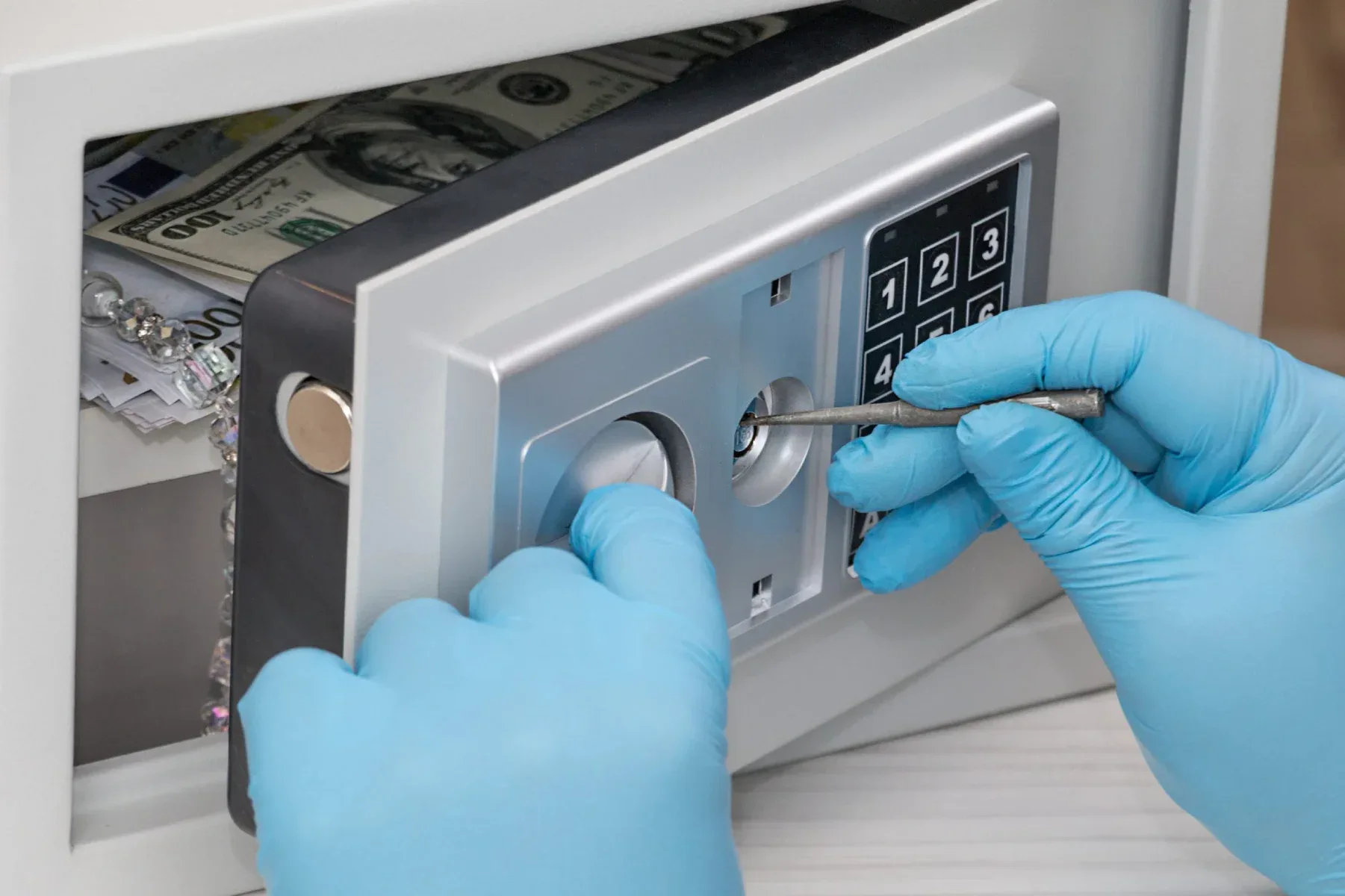Hands in blue gloves opening a safe with money inside