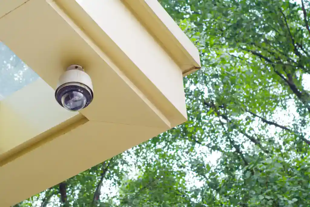 Security camera mounted on a building with green trees in the background