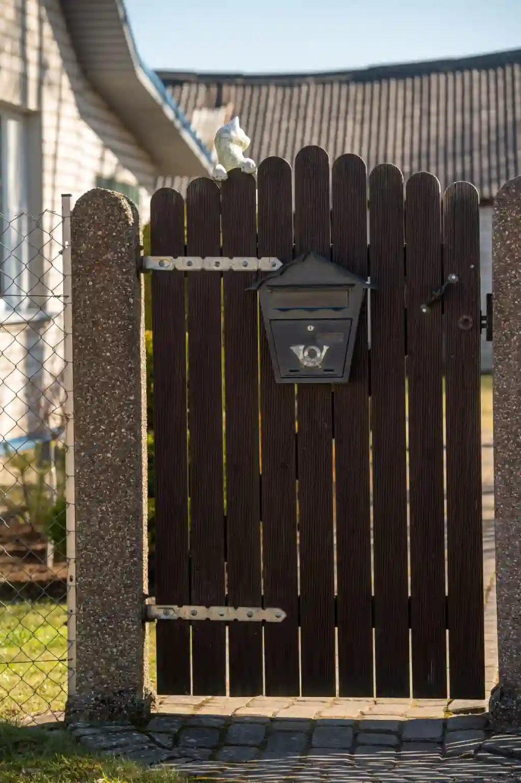 Dark wooden gate with a black mailbox and a white decorative figure.