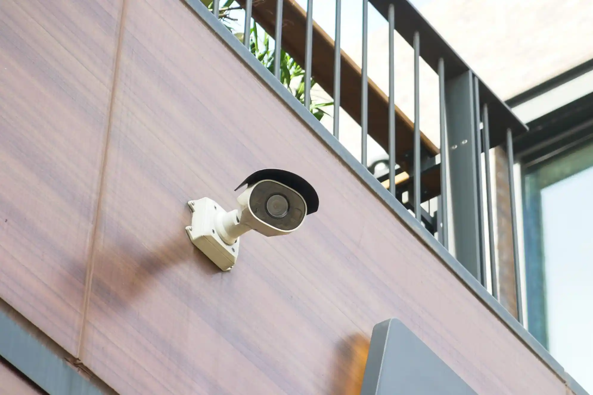 White and black security camera mounted on a wooden wall.