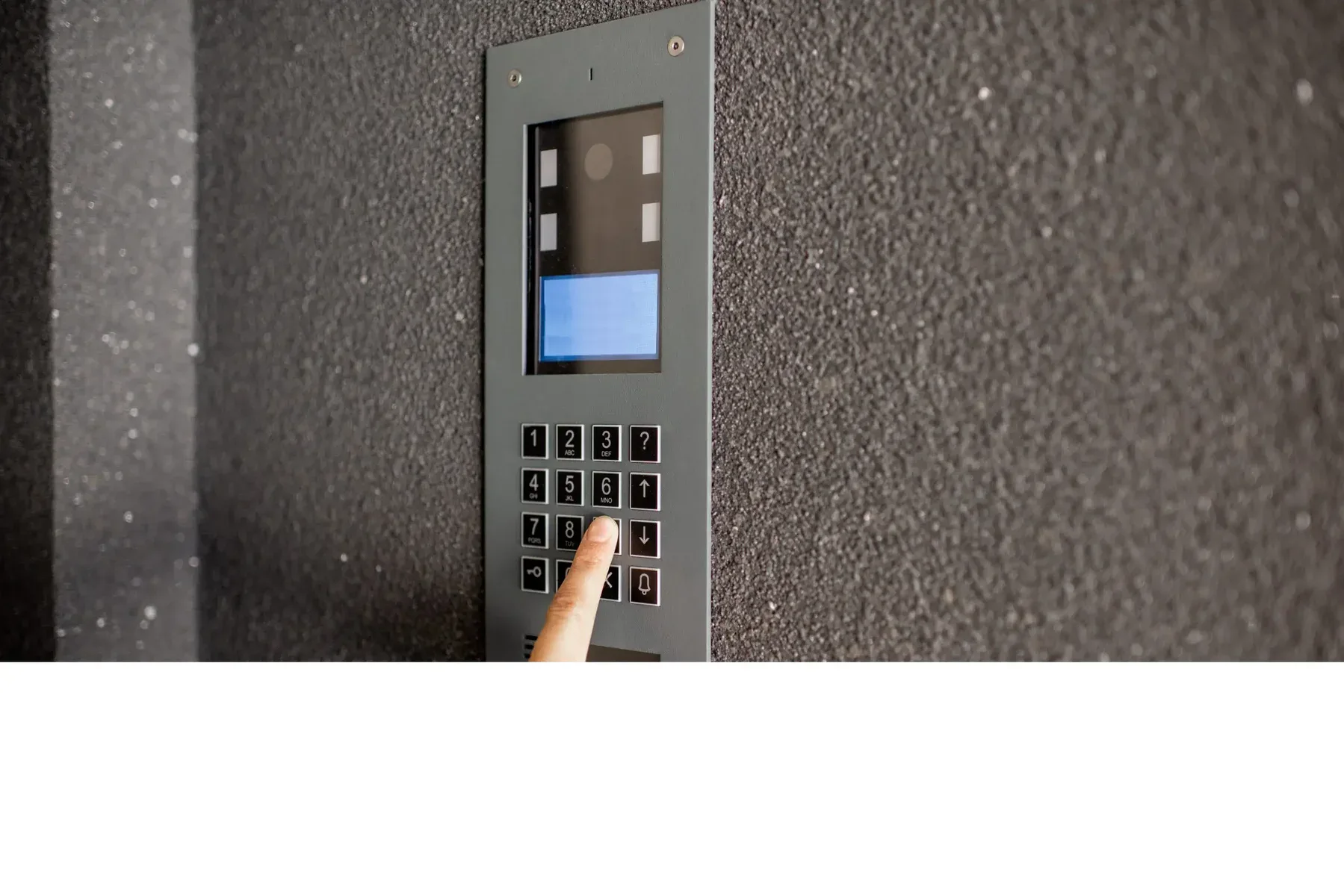 Finger pressing button on a modern intercom system on a textured wall