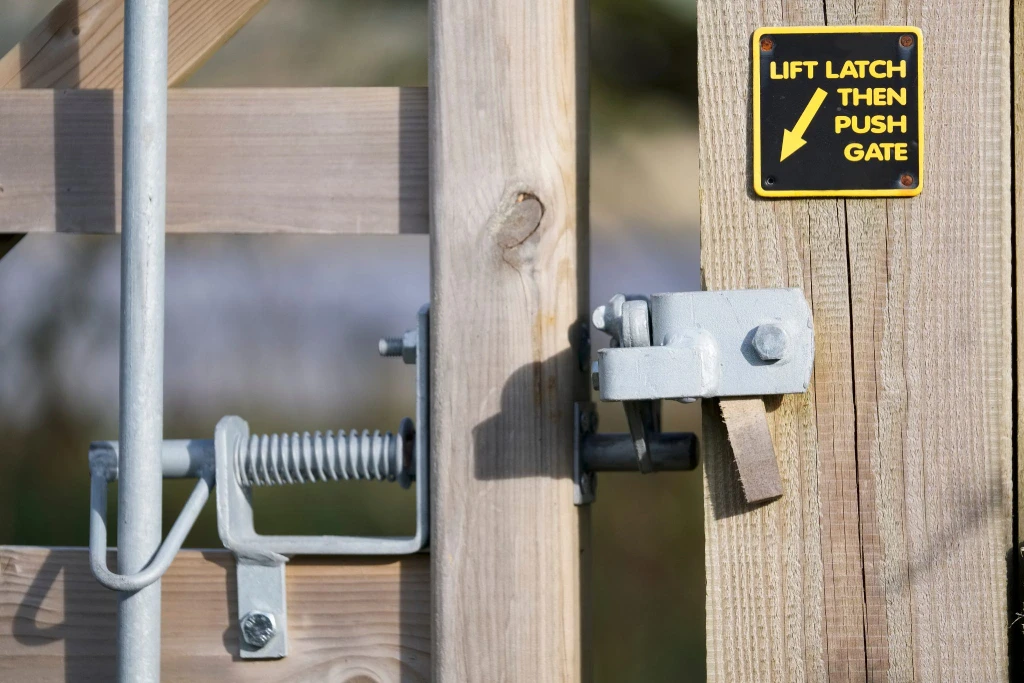 Close-up of a wooden gate with a metal latch and a yellow sign.